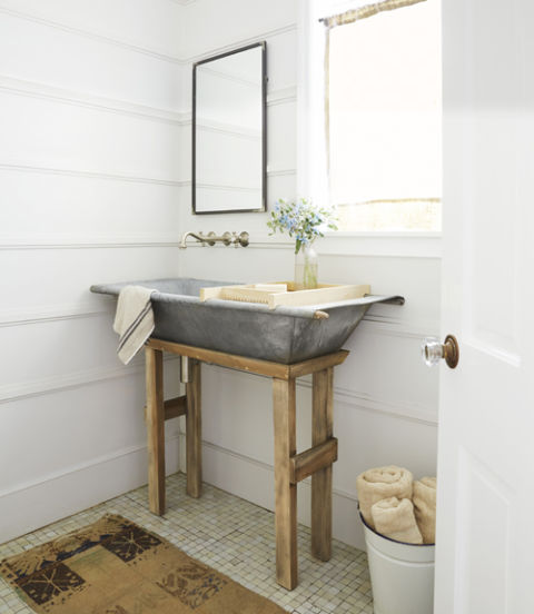 A simple wooden stand (and holes drilled for plumbing) transforms a Dutch galvanized metal hay-collecting bin into a statement-making sink in this California cottage's powder room.
