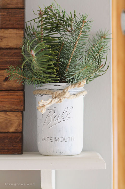 Use a distressed-white Mason jar, bits of evergreen, and some rope to add visual interest to a kitchen shelf. See more at Love Grows Wild. 