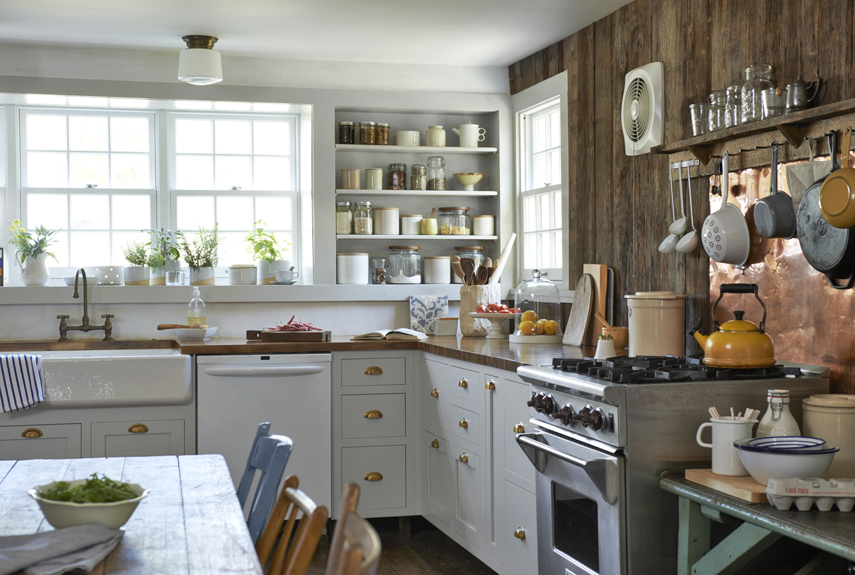 Switching out the stainless steel sink that came with the house for an apron-front porcelain one boosts the room's charm. Brass bin pulls, butcher block countertops, and a copper backsplash behind the range add warmth to the new gray cabinets.
